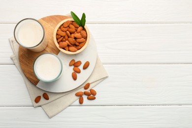 Photo of Glasses of almond milk and almonds on white wooden table, top view. Space for text