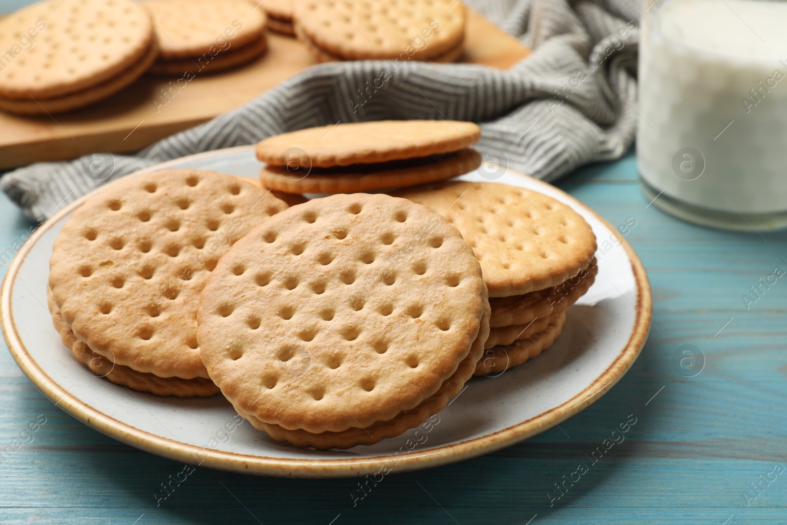 Photo of Tasty sandwich cookies and glass of milk on light blue wooden table, closeup