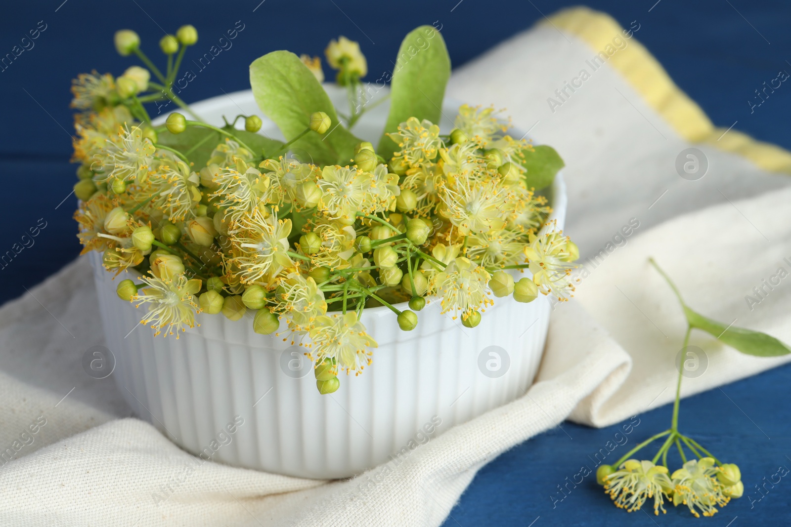 Photo of Fresh linden leaves and flowers in bowl on blue wooden table