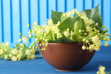 Photo of Fresh linden leaves and flowers in bowl on blue wooden table