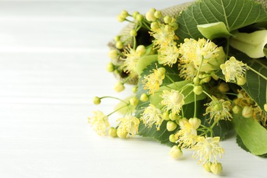 Photo of Fresh linden leaves and flowers on white wooden table, closeup. Space for text