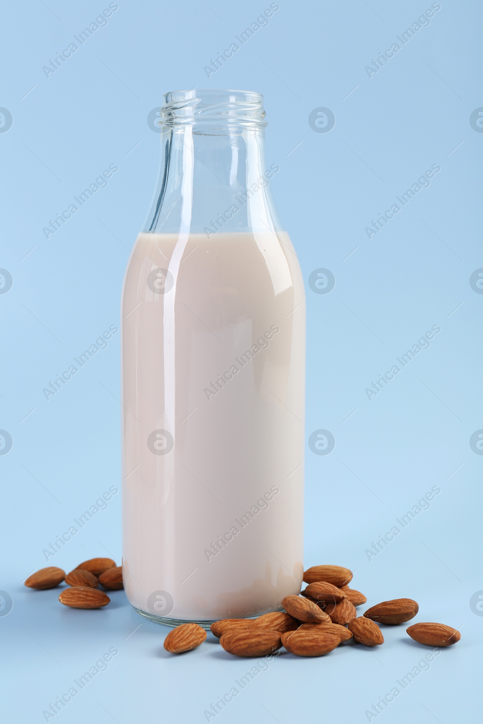 Photo of Fresh almond milk in glass bottle and nuts on light blue background