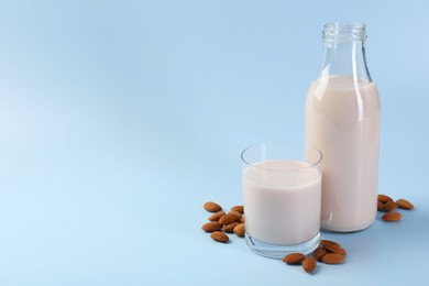 Photo of Fresh almond milk in bottle, glass and nuts on light blue background, space for text