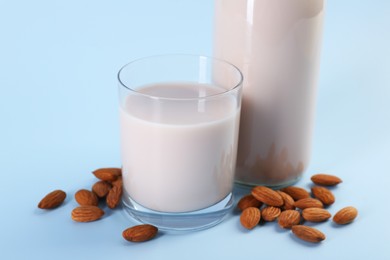 Fresh almond milk in glass, bottle and nuts on light blue background