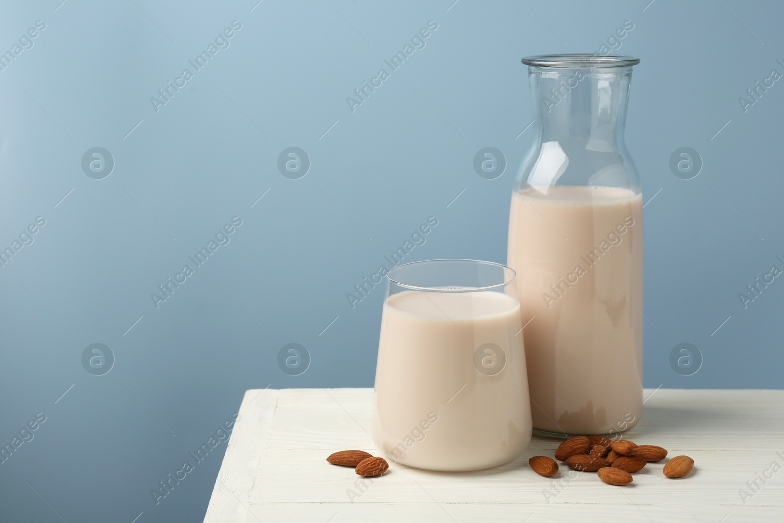 Photo of Fresh almond milk in carafe, glass and nuts on white wooden table, space for text