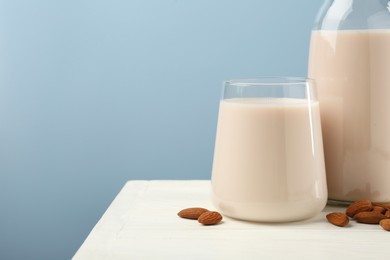 Photo of Fresh almond milk in glass, bottle and nuts on white wooden table, space for text