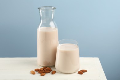 Fresh almond milk in carafe, glass and nuts on white wooden table