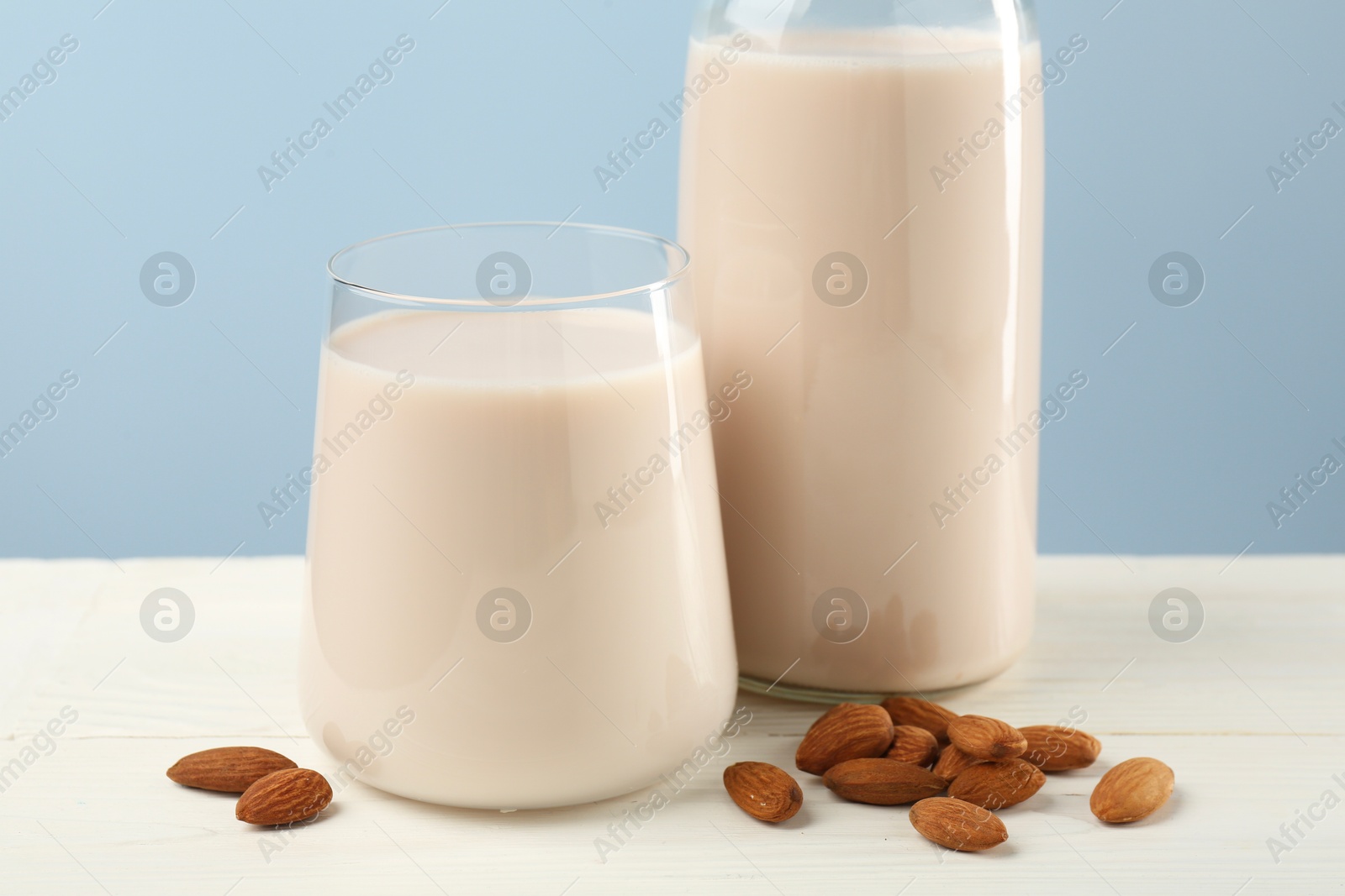 Photo of Fresh almond milk in glass, bottle and nuts on white wooden table