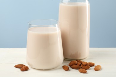 Photo of Fresh almond milk in glass, bottle and nuts on white wooden table