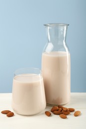 Photo of Fresh almond milk in carafe, glass and nuts on white wooden table