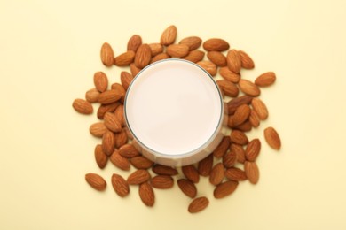 Fresh almond milk in glass and nuts on beige background, top view