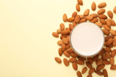 Fresh almond milk in glass and nuts on beige background, top view. Space for text