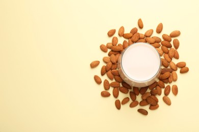 Photo of Fresh almond milk in glass and nuts on beige background, top view. Space for text