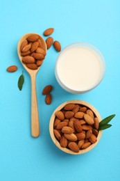 Fresh almond milk in glass, nuts, spoon and green leaves on light blue background, flat lay