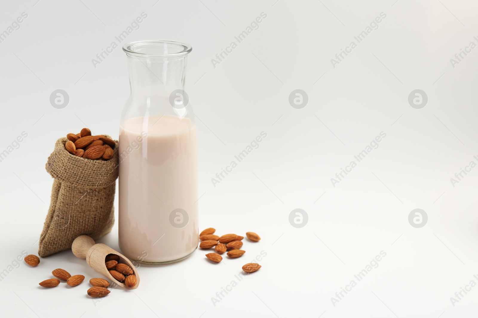 Photo of Fresh almond milk in carafe, nuts, scoop and burlap sack on white background, space for text