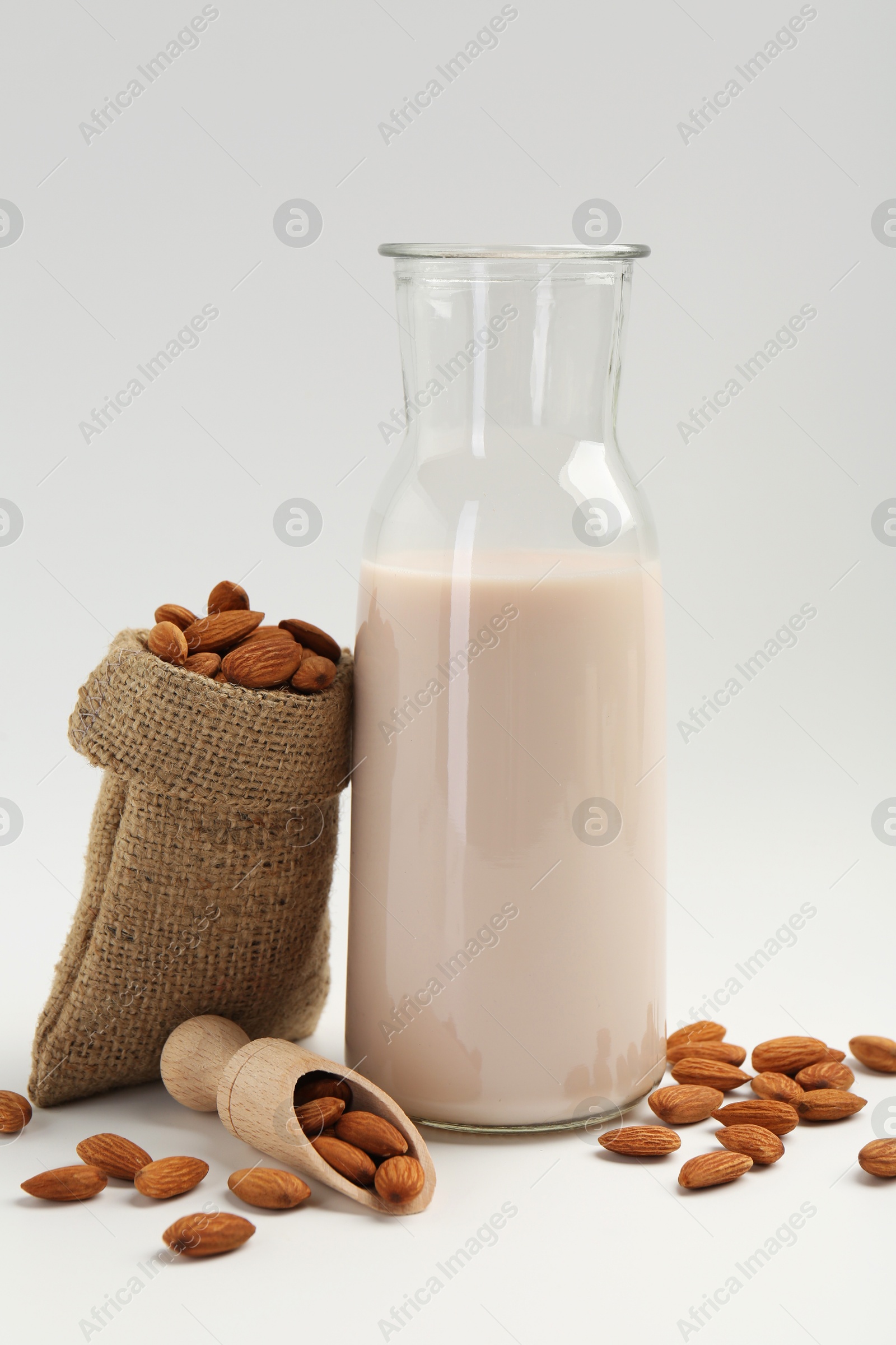 Photo of Fresh almond milk in carafe, nuts, scoop and burlap sack on white background