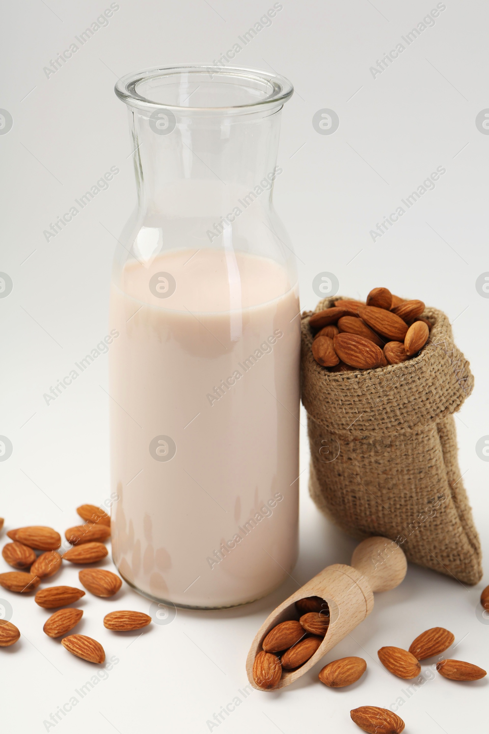 Photo of Fresh almond milk in carafe, nuts, scoop and burlap sack on white background