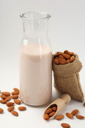 Photo of Fresh almond milk in carafe, nuts, scoop and burlap sack on white background