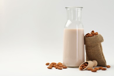 Photo of Fresh almond milk in carafe, nuts, scoop and burlap sack on white background, space for text