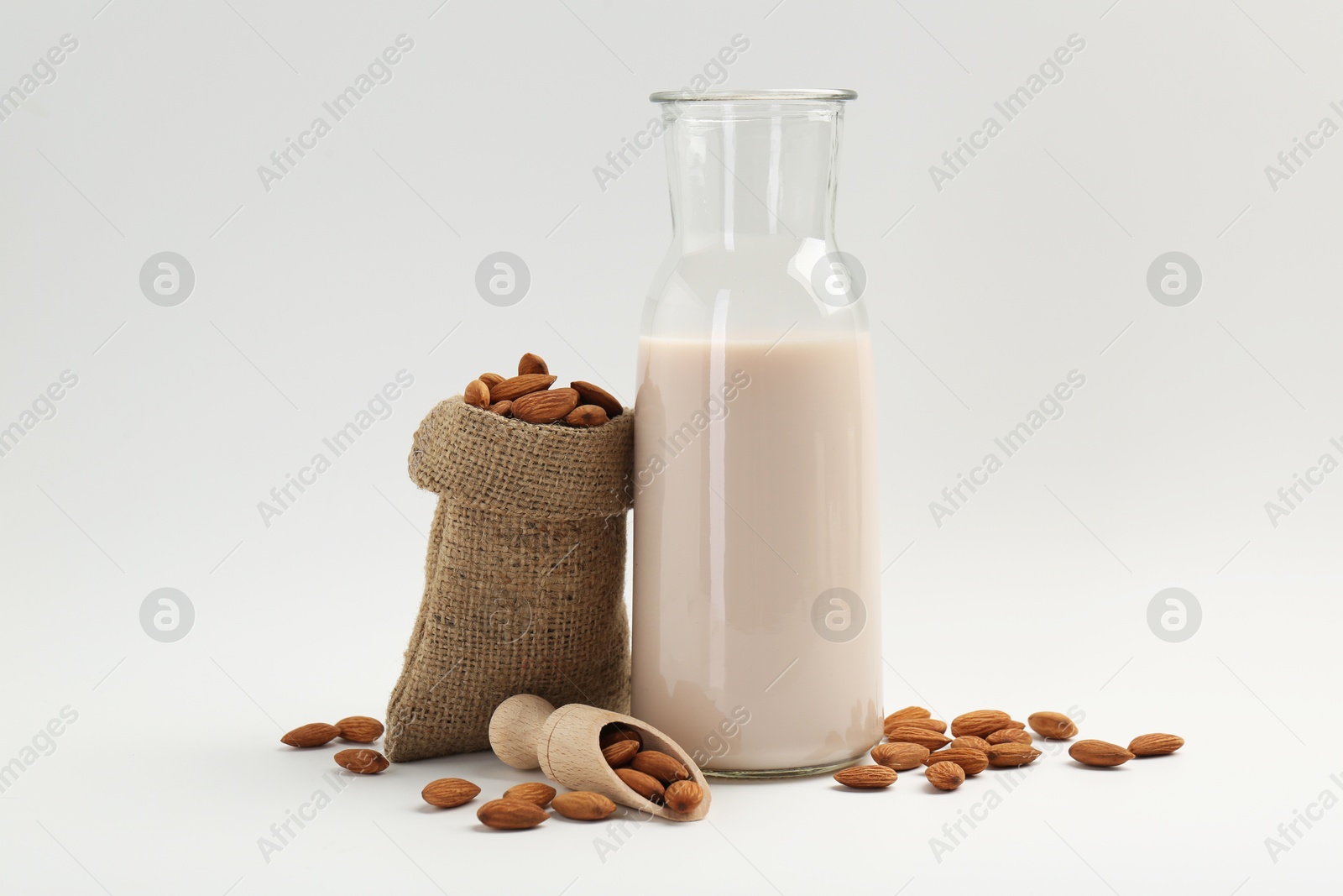 Photo of Fresh almond milk in carafe, nuts, scoop and burlap sack on white background