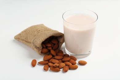 Photo of Fresh almond milk in glass, nuts and burlap sack on white background