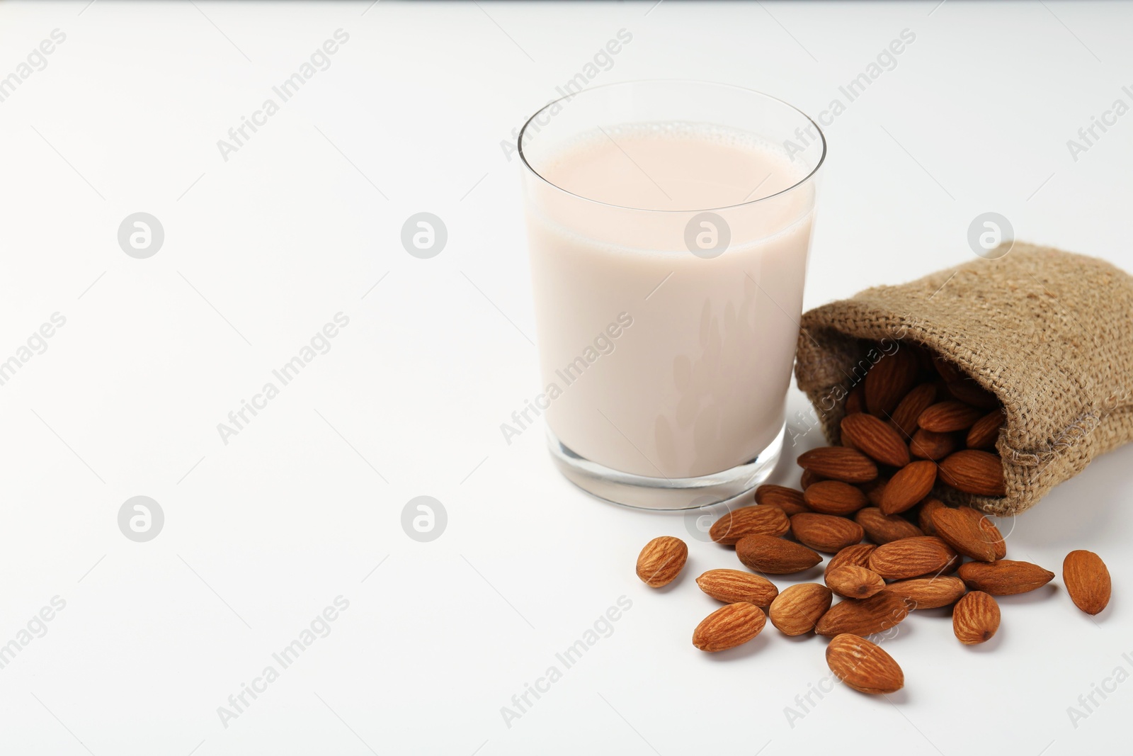 Photo of Fresh almond milk in glass, nuts and burlap sack on white background, space for text