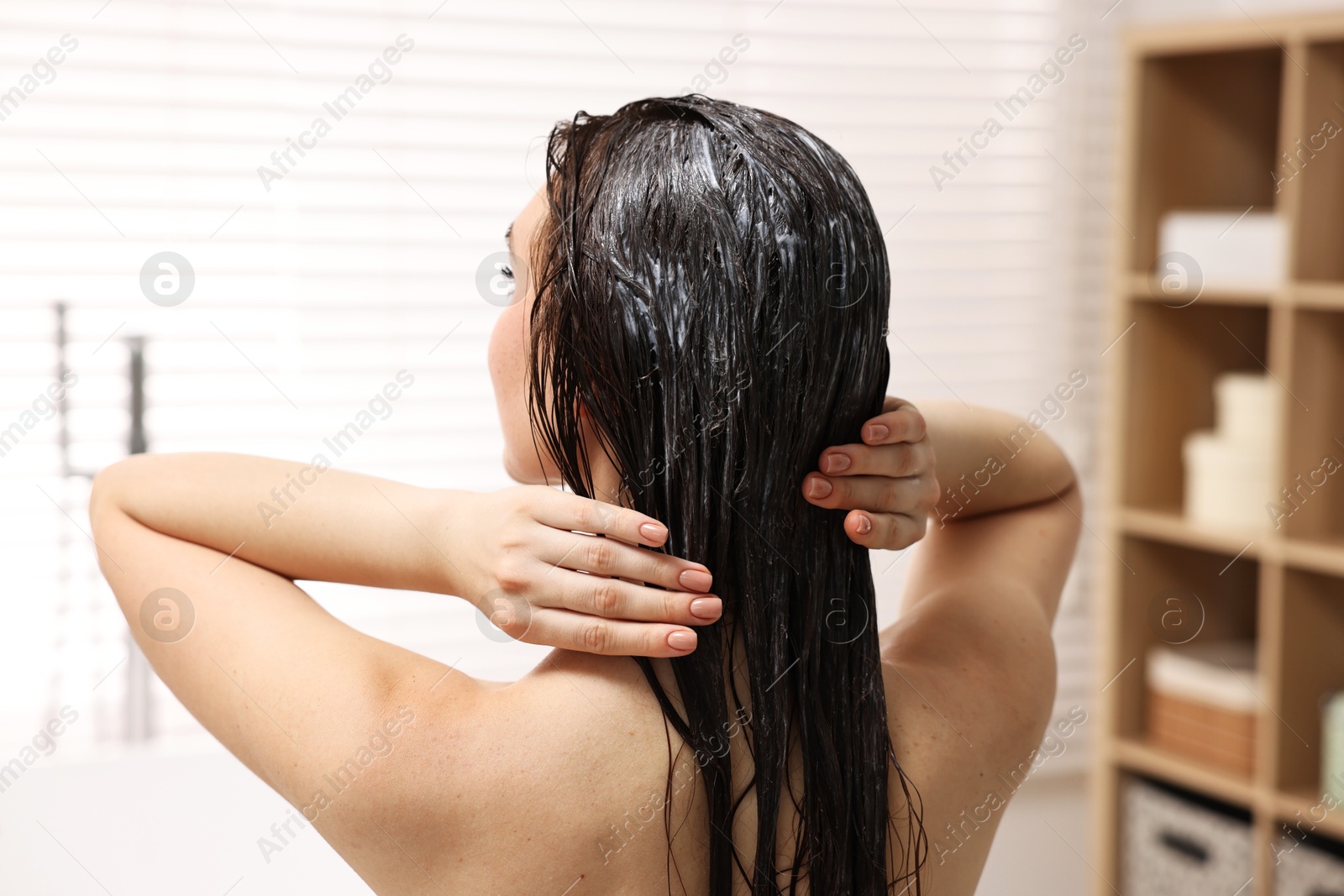 Photo of Woman applying hair mask in bathroom, back view