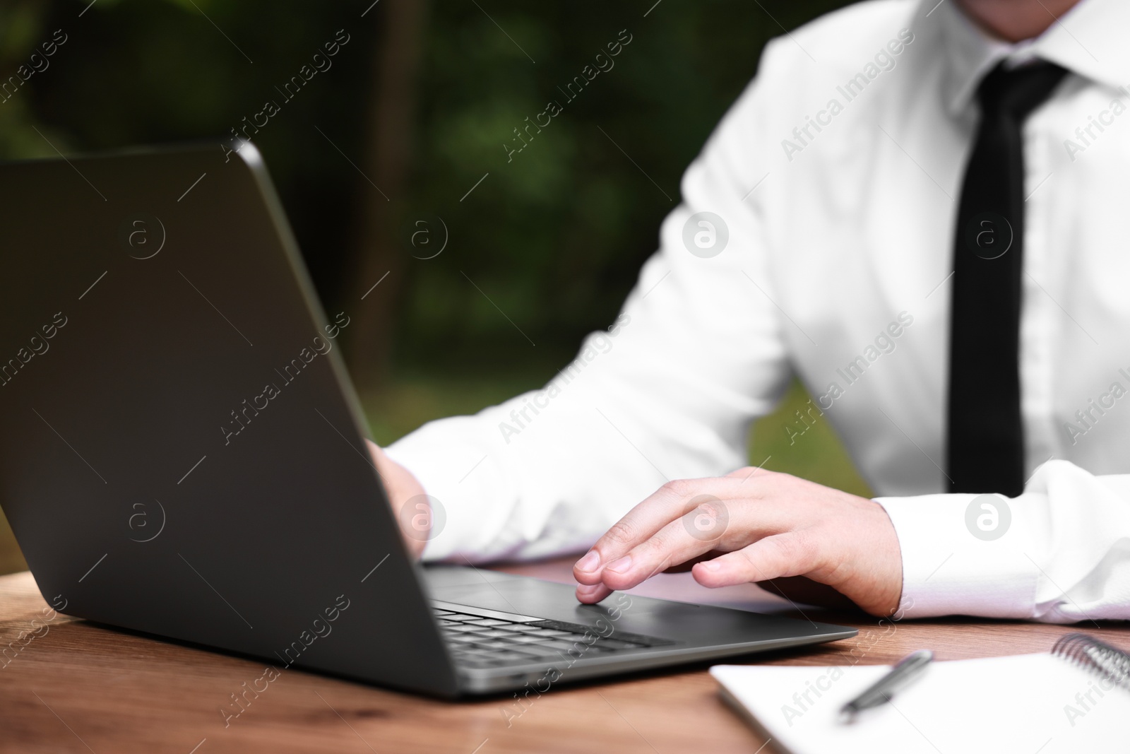 Photo of Businessman working with laptop at table outdoors, closeup. Remote job