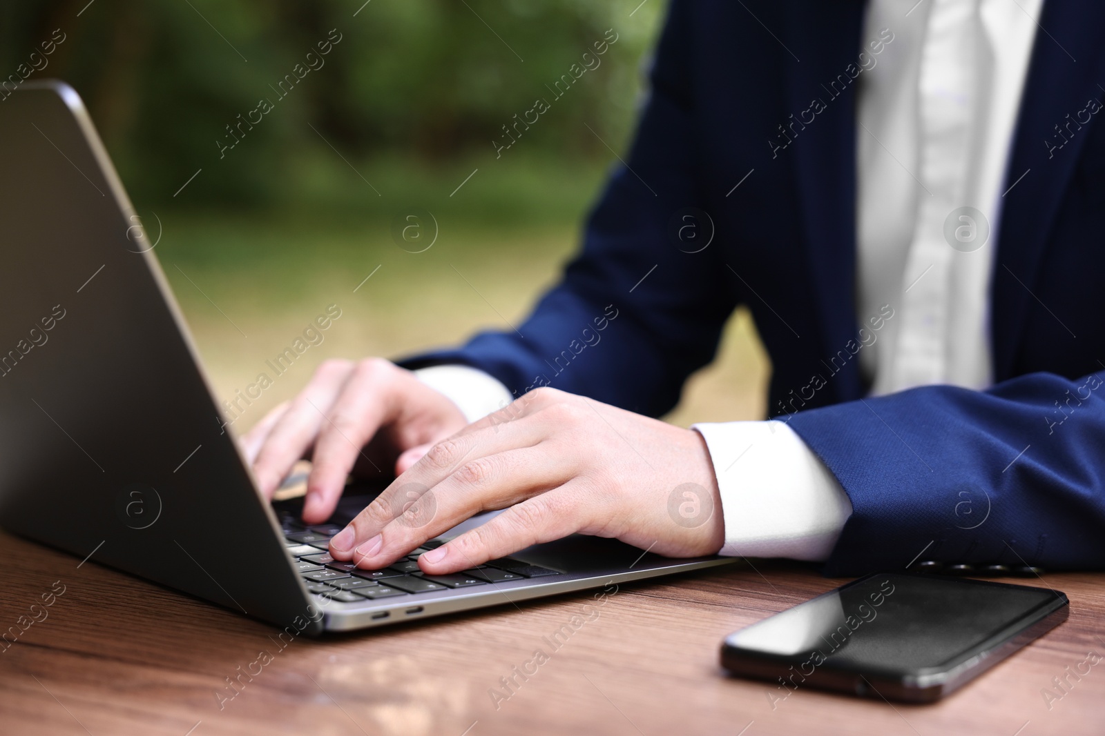 Photo of Businessman working with laptop at table outdoors, closeup. Remote job