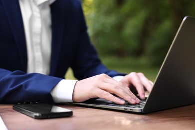 Photo of Businessman working with laptop at table outdoors, closeup. Remote job