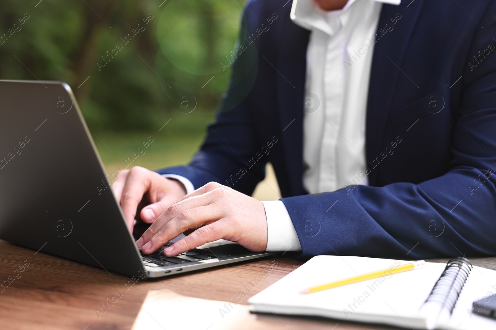 Photo of Businessman working with laptop at table outdoors, closeup. Remote job