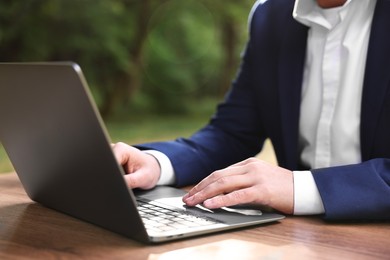 Photo of Businessman working with laptop at table outdoors, closeup. Remote job