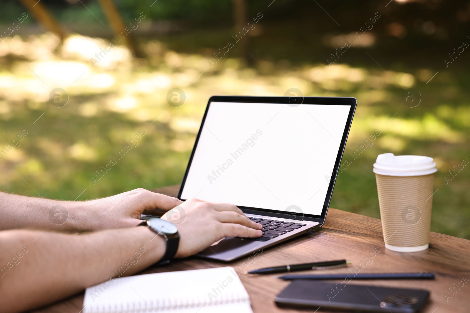 Photo of Freelancer working with laptop at wooden table outdoors, closeup. Remote job