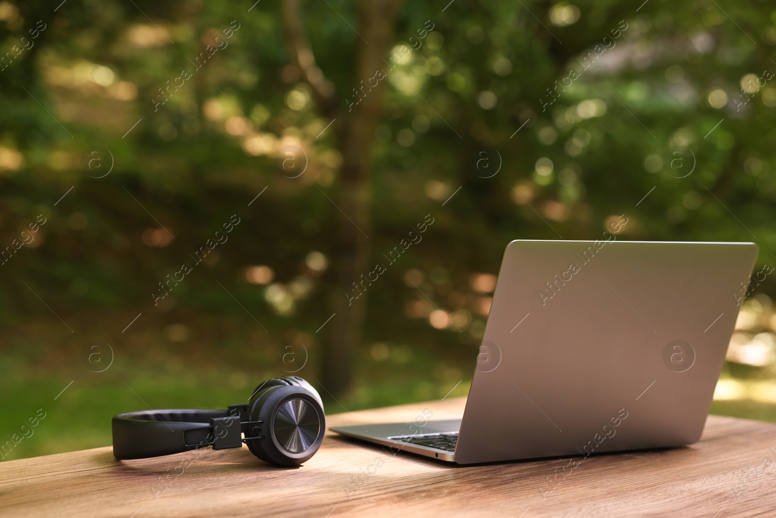 Photo of Laptop and headphones on wooden table outdoors. Remote work