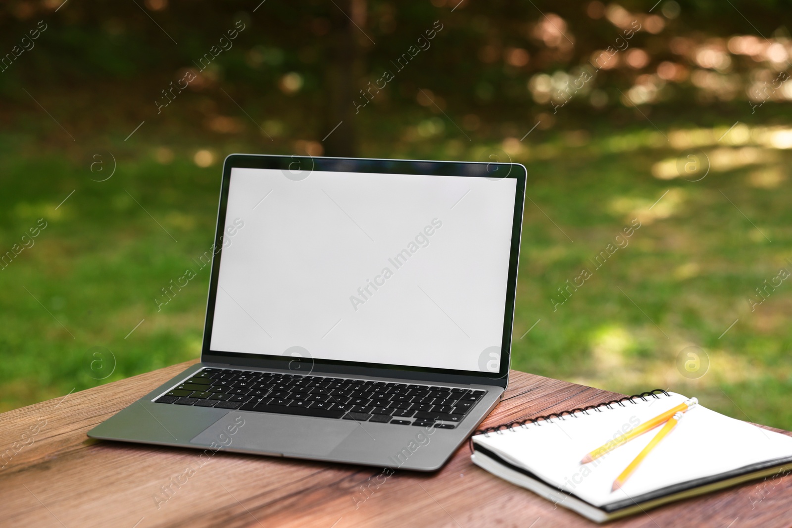 Photo of Laptop, notebook and pencils on wooden table outdoors. Remote work