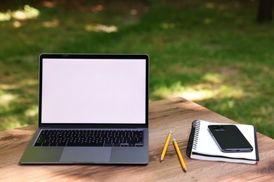 Photo of Laptop, notebook, pencils and smartphone on wooden table outdoors. Remote work