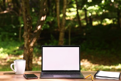 Photo of Laptop, notebook, pencils, cup and smartphone on wooden table outdoors. Remote work