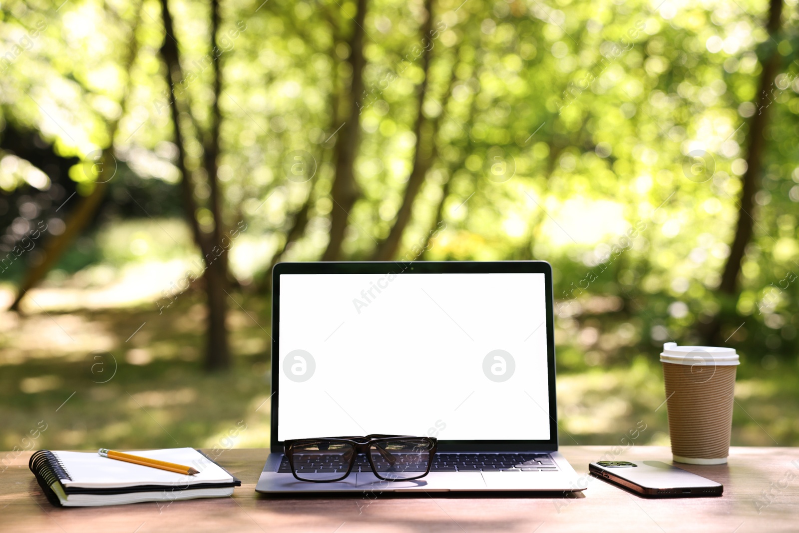 Photo of Laptop, glasses and smartphone on wooden table outdoors. Remote work