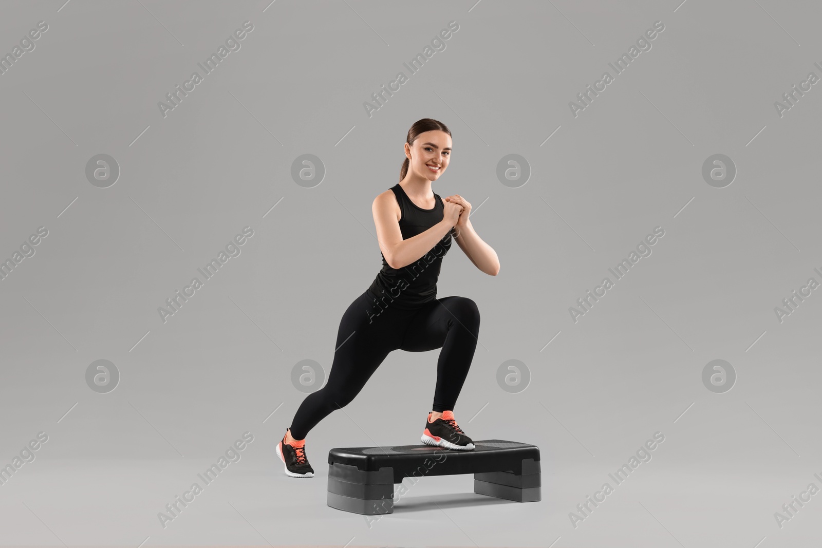 Photo of Young woman doing aerobic exercise with step platform on light background