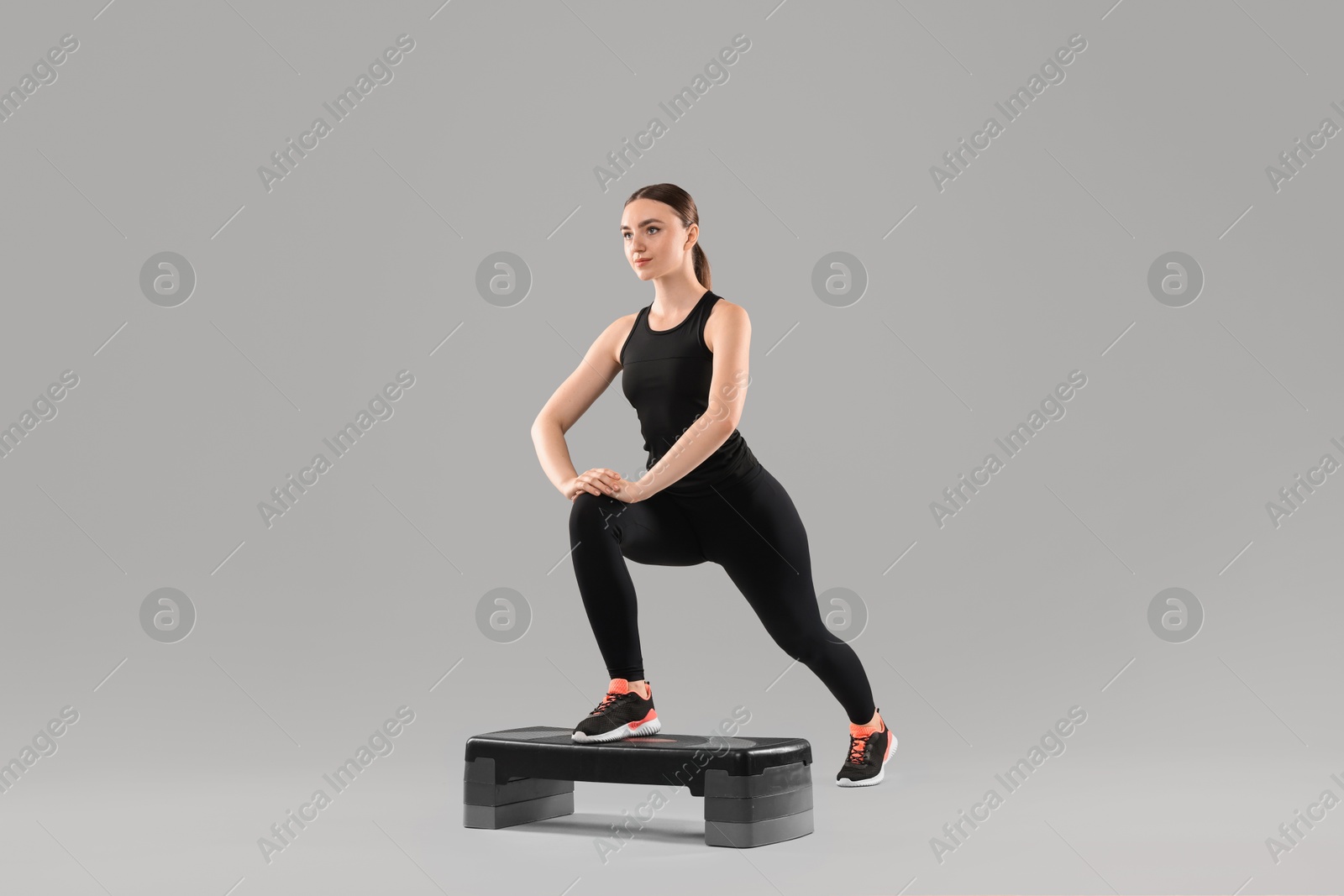 Photo of Young woman doing aerobic exercise with step platform on light background