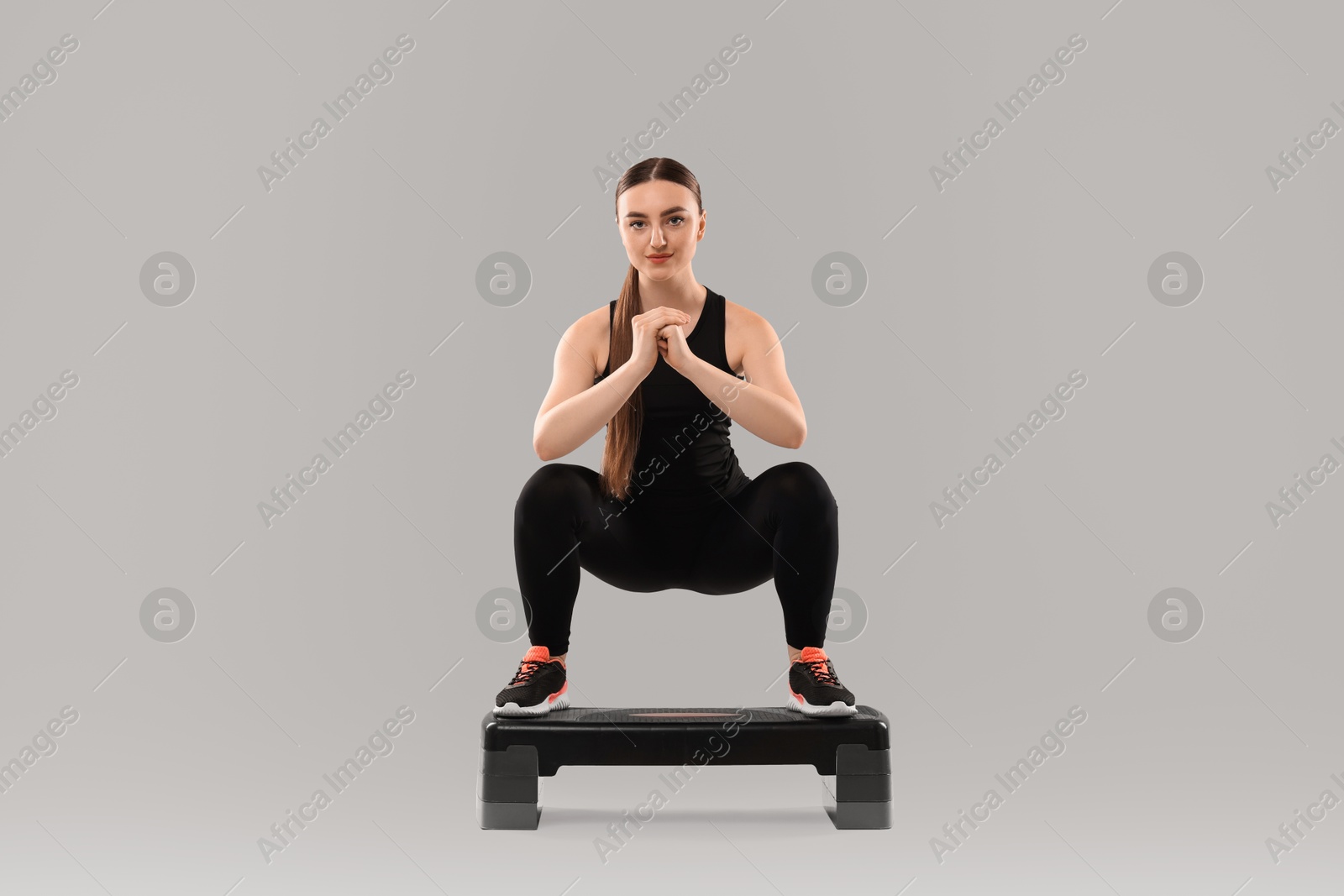 Photo of Young woman doing aerobic exercise with step platform on light background