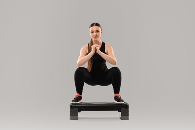 Photo of Young woman doing aerobic exercise with step platform on light background