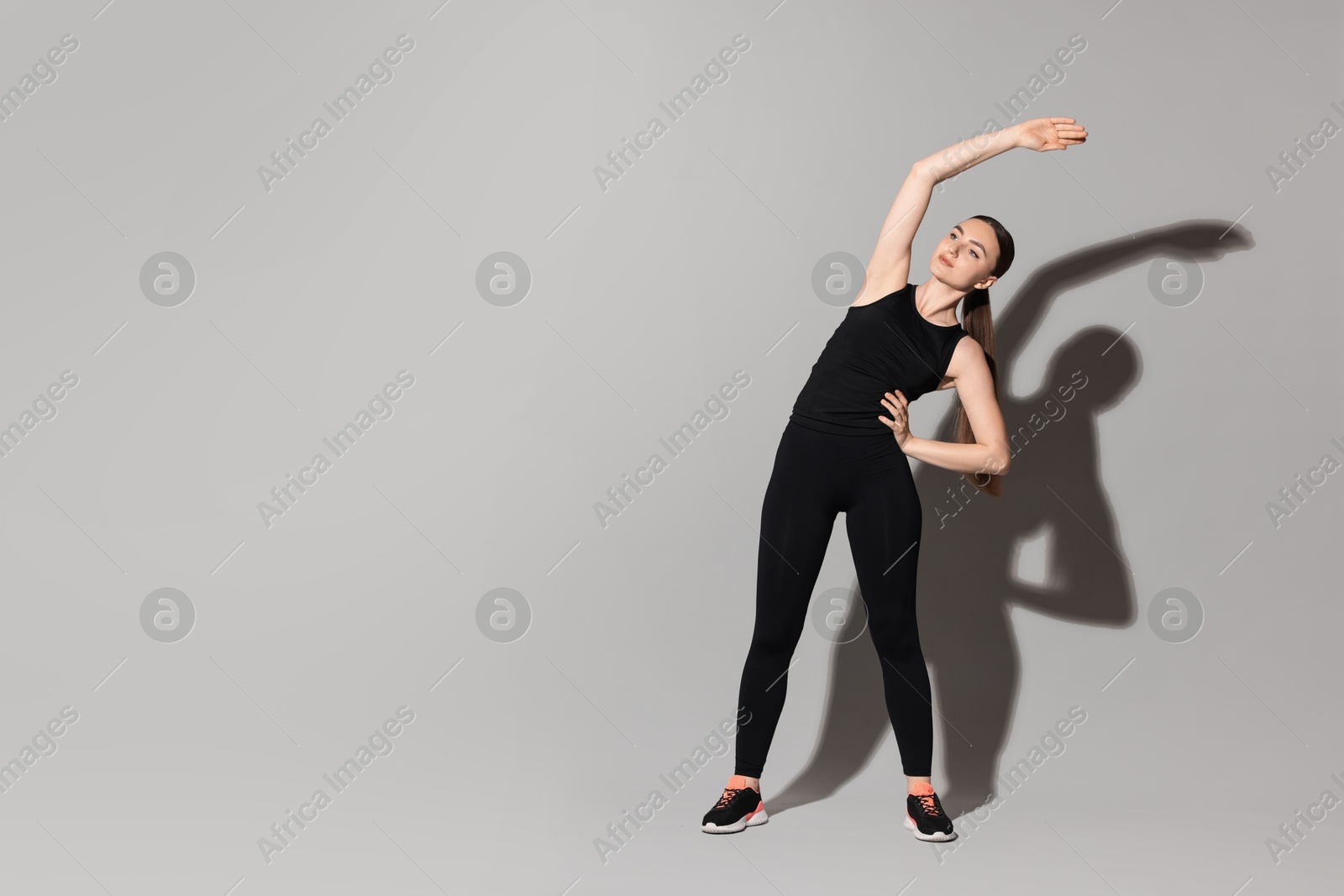 Photo of Aerobics. Young woman doing stretching exercise on light grey background, space for text