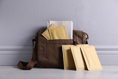 Photo of Brown postman's bag with envelopes and newspapers near grey wall