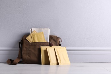 Brown postman's bag with envelopes and newspapers near grey wall. Space for text