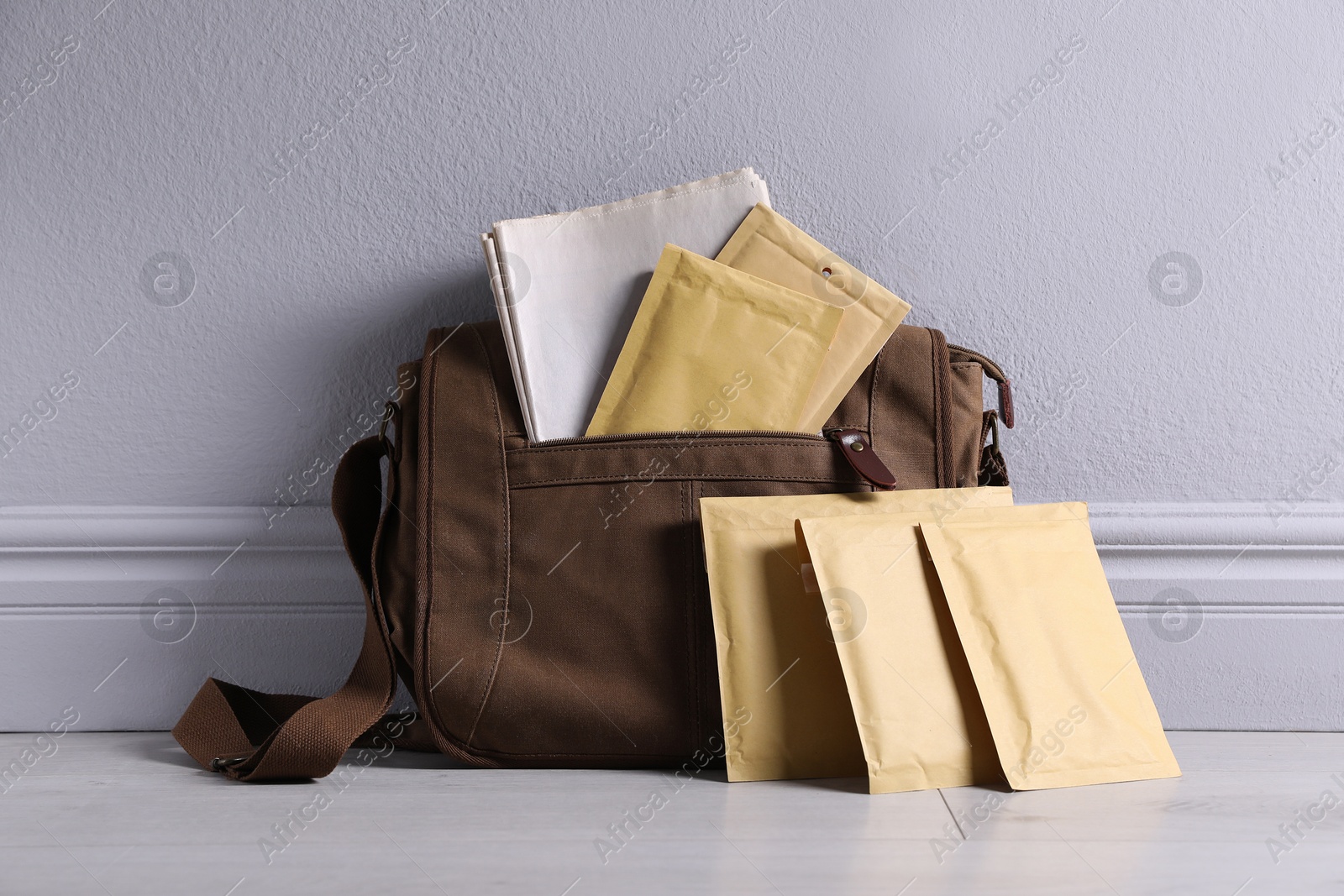 Photo of Brown postman's bag with envelopes and newspapers near grey wall