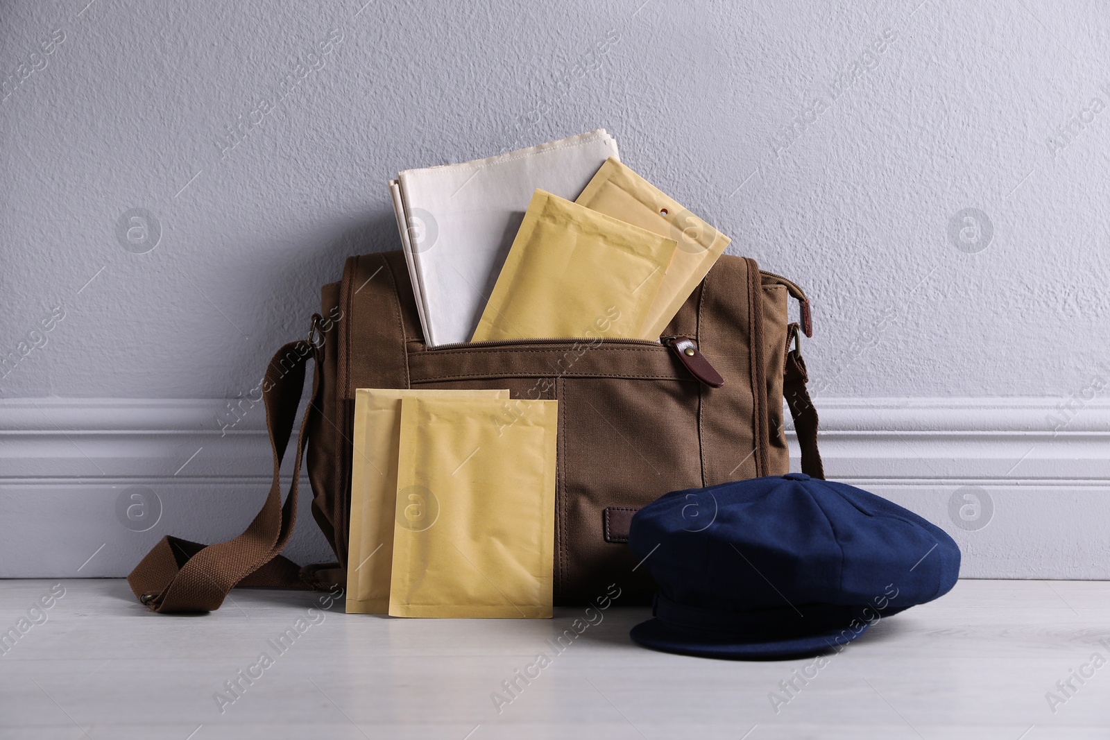 Photo of Brown postman's bag, envelopes, newspapers and hat near grey wall