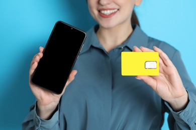 Photo of Woman holding SIM card and smartphone on light blue background, closeup