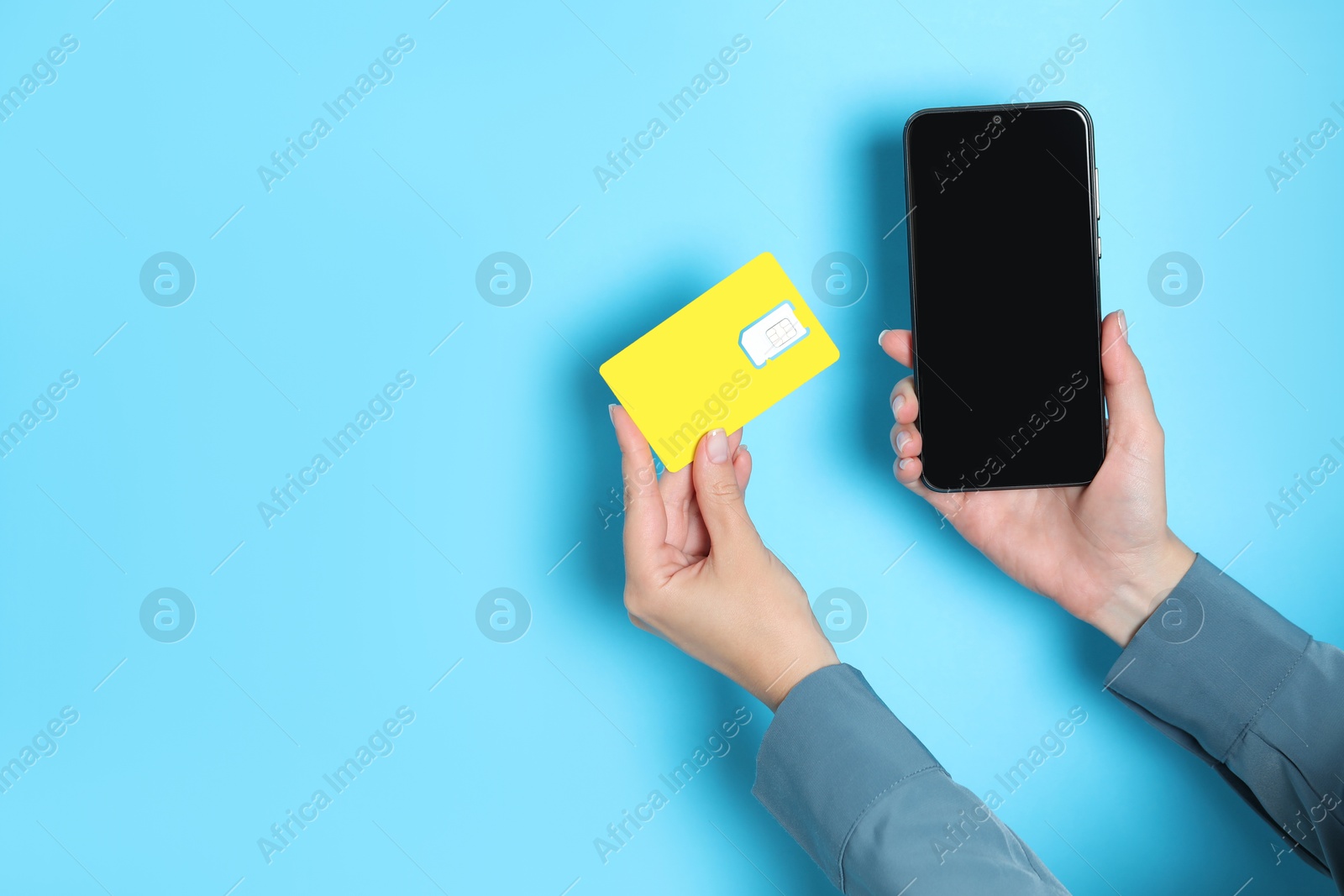 Photo of Woman holding SIM card and smartphone on light blue background, closeup. Space for text