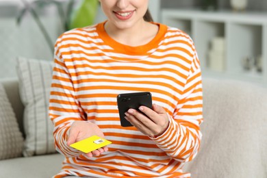 Photo of Woman holding SIM card and smartphone on sofa indoors, closeup